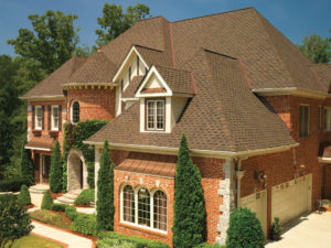 A large brick home with brown asphalt shingle roofing and manicured landscaping 